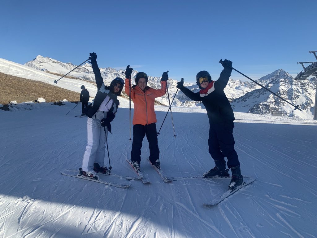 3 students with their arms and ski poles in the air
