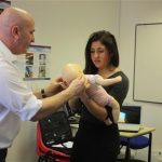 teacher helping pupil hold a fake baby doll