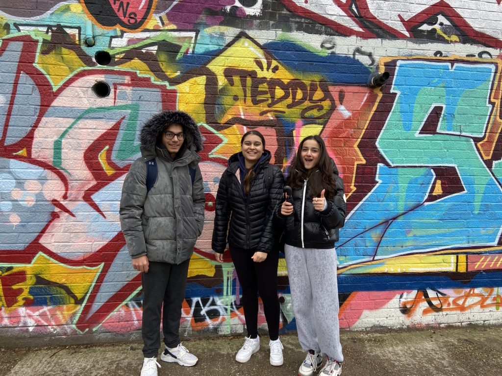 3 College students stood behind a wall of graffiti