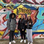 3 College students stood behind a wall of graffiti