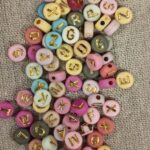 Pile of pastel wooden beads with gold-letter engravings scattered on burlap fabric.
