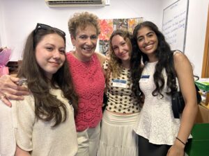 Four smiling women posing closely for a selfie at an indoor event, wearing name badges.